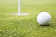 Photo: Golf ball on a putting green with the flag in background Golf ball on a putting green with the flag in background