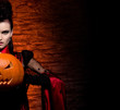 A young brunette vampire lady holding a pumpkin