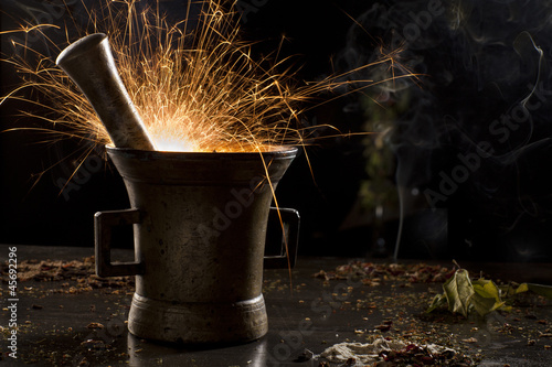 Photo: metal mortar with sparkling fire, surrounded with spices metal mortar with sparkling fire, surrounded with spices