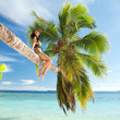 Fashion woman siting upon palm tree on the beach
