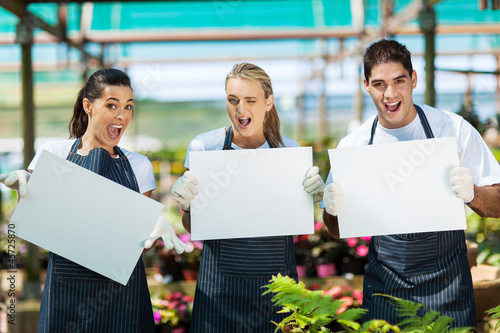 Photo: group of funny nursery workers with white board in greenhouse group of funny nursery workers with white board in greenhouse