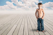 Young kid standing on a wood floor with cloudy blue sky.