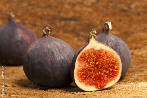 Photo: Two whole and a halved fig fruits on bark as background Two whole and a halved fig fruits on bark as background