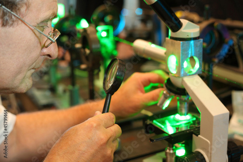Photo: Scientist with glass, loupe configure laser of microparticles Scientist with glass, loupe configure laser of microparticles