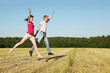 Husband, wife jumping in field near wood, side