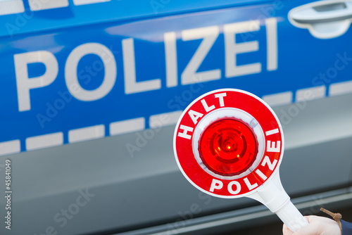 Photo: Polizist hält Polizeikelle vor Polizeiauto Polizist hält Polizeikelle vor Polizeiauto