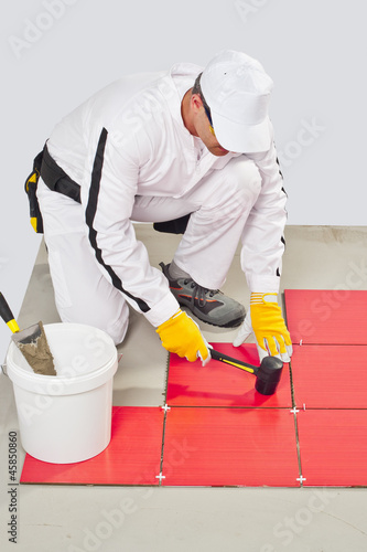 Photo: Worker Applies with Rubber Hummer Red Tile on a Floor Worker Applies with Rubber Hummer Red Tile on a Floor