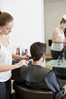 A female hairdresser cutting male clients hair with scissors