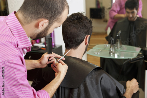 Photo: A male hairdresser cutting his male clients hair with scissors A male hairdresser cutting his male clients hair with scissors
