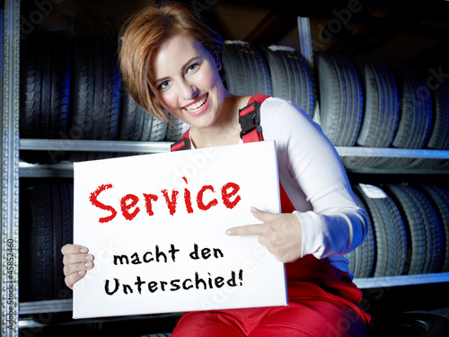 Photo: Female car mechanic presents white message board in a tire stock Female car mechanic presents white message board in a tire stock