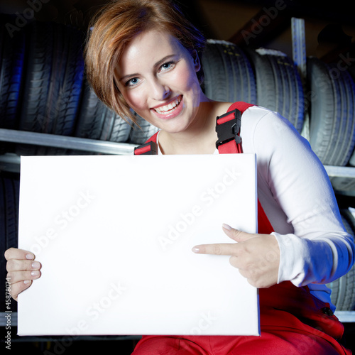 Photo: Female car mechanic presenting white message board in a garage Female car mechanic presenting white message board in a garage