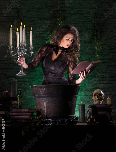 Photo: A young brunette witch in a dark dress making a mystical posion A young brunette witch in a dark dress making a mystical posion