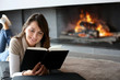 canvas print picture - Portrait of beautiful woman reading book by fireplace
