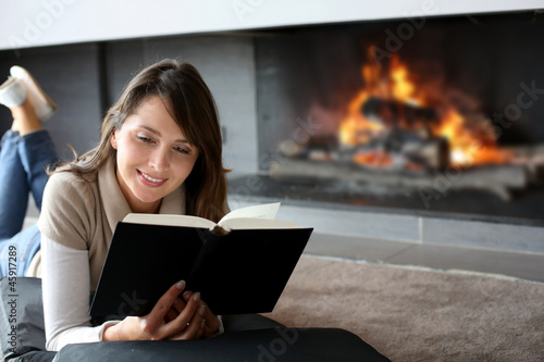 Photo: Portrait of beautiful woman reading book by fireplace Portrait of beautiful woman reading book by fireplace