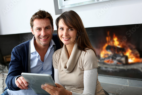 Photo: Couple sitting by fireplace and websurfing with tablet Couple sitting by fireplace and websurfing with tablet