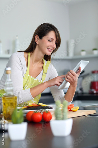 Photo: Woman in kitchen looking for dish recipe on internet Woman in kitchen looking for dish recipe on internet