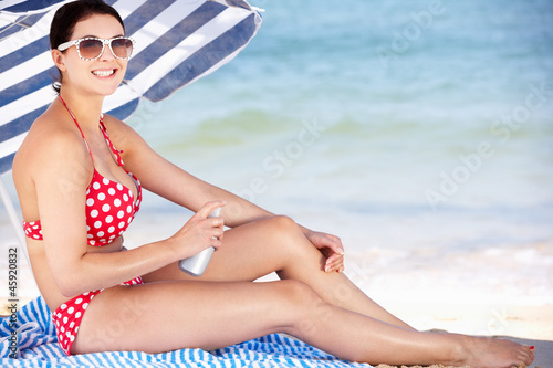 Photo: Woman Sheltering From Sun Under Beach Umbrella Putting On Sun Cr Woman Sheltering From Sun Under Beach Umbrella Putting On Sun Cr