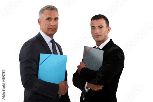 Photo: Two businessmen standing and holding files. Two businessmen standing and holding files.
