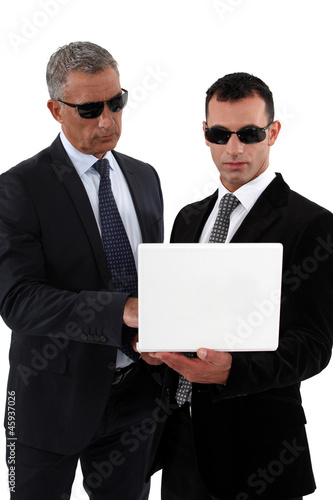 Photo: Businessmen wearing sunglasses and looking at a laptop Businessmen wearing sunglasses and looking at a laptop