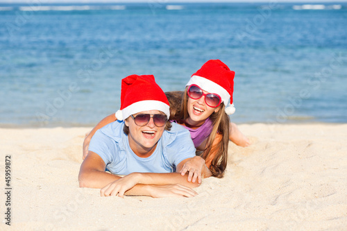 Photo: beautiful couple in santa hats on tropical beach of Bali beautiful couple in santa hats on tropical beach of Bali
