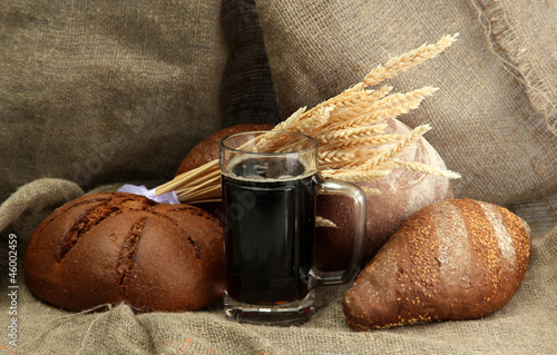 Photo: tankard of kvass and rye breads with ears, on burlap background tankard of kvass and rye breads with ears, on burlap background