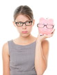 Upset woman wearing glasses holding piggy bank