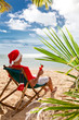 Photo: Man in Santa's hat with cocktail sitting on chair on a beach Man in Santa's hat with cocktail sitting on chair on a beach