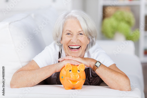 Photo: lachende seniorin mit ihrem sparschwein lachende seniorin mit ihrem sparschwein