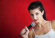 Photo: Beautiful girl singing with microphone against red background Beautiful girl singing with microphone against red background