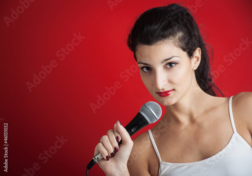 Photo: Beautiful girl singing with microphone against red background Beautiful girl singing with microphone against red background