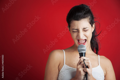 Photo: Beautiful girl singing with microphone against red background Beautiful girl singing with microphone against red background