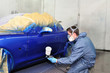 Worker painting a car in paint booth.