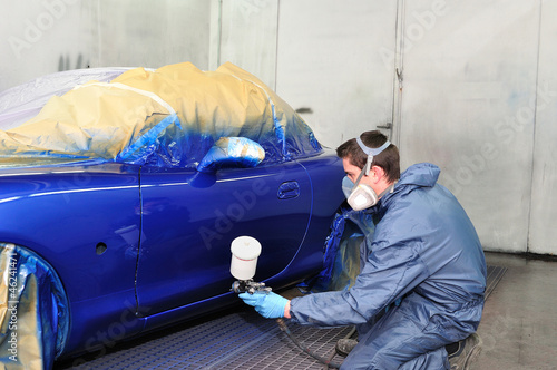 Photo: Worker painting a car in paint booth. Worker painting a car in paint booth.