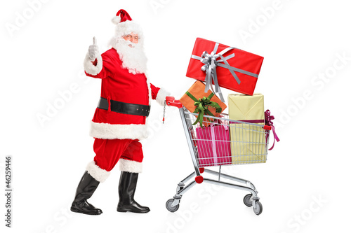 Photo: Santa Claus pushing a shopping cart full of gifts and giving a t Santa Claus pushing a shopping cart full of gifts and giving a t