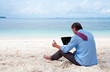 Photo: Business man sitting and working on the beach with tablet comput Business man sitting and working on the beach with tablet comput