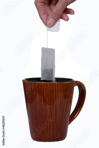 Photo: Hand holding teabag above ceramic mug. Hand holding teabag above ceramic mug.