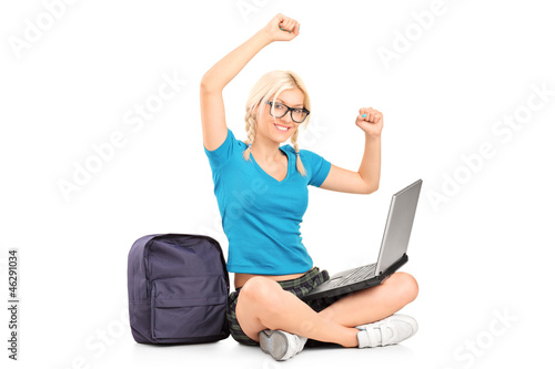 Photo: A happy female student seated on a floor working on a laptop A happy female student seated on a floor working on a laptop