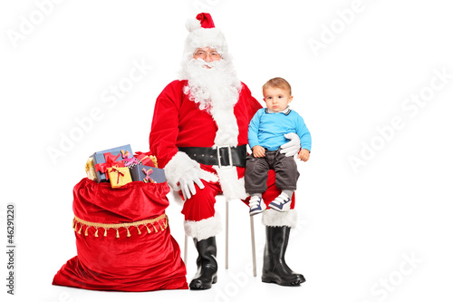 Photo: Santa Claus and small child on his lap posing next to a bag full Santa Claus and small child on his lap posing next to a bag full