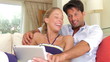 Couple Sitting On Sofa Using Digital Tablet