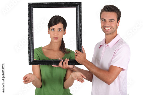 Photo: Playful couple stood with empty picture frame Playful couple stood with empty picture frame