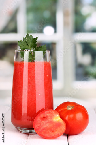 Photo: Glass of tomato juice on wooden table, on window background Glass of tomato juice on wooden table, on window background