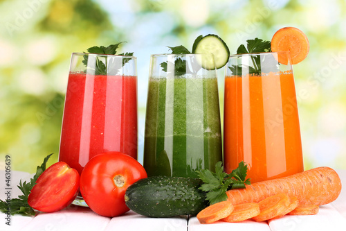 Photo: Fresh vegetable juices on wooden table, on green background Fresh vegetable juices on wooden table, on green background