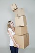 Smiling young woman holding a stack of falling carton boxes