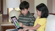 Young boy and girl on sofa using digital tablet to read Spanish language book