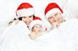 Christmas family with baby smiling in red hat in white bed