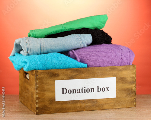 Photo: Donation box with clothing on red background close-up Donation box with clothing on red background close-up