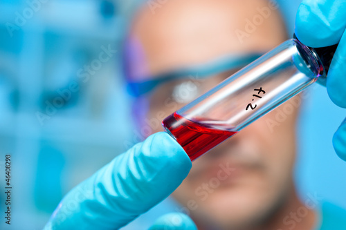Photo: Gloved hands hold transparent sample tube Gloved hands hold transparent sample tube