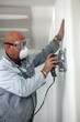 Man wearing mask and goggles whilst sanding wall