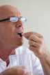 Elderly man swallowing a pill