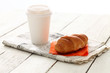 Still hot coffee with fresh croissant on newspaper over wooden s